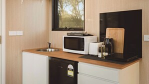 A compact kitchen with a microwave, toaster, coffee maker, and a black induction cooktop. - Rowsley Valley Tiny House 1 by Tiny Away (Glenmore)