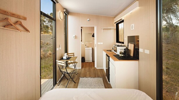 A compact, modern room with a bed, a small kitchenette, and a dining area. - Rowsley Valley Tiny House 1 by Tiny Away (Glenmore)