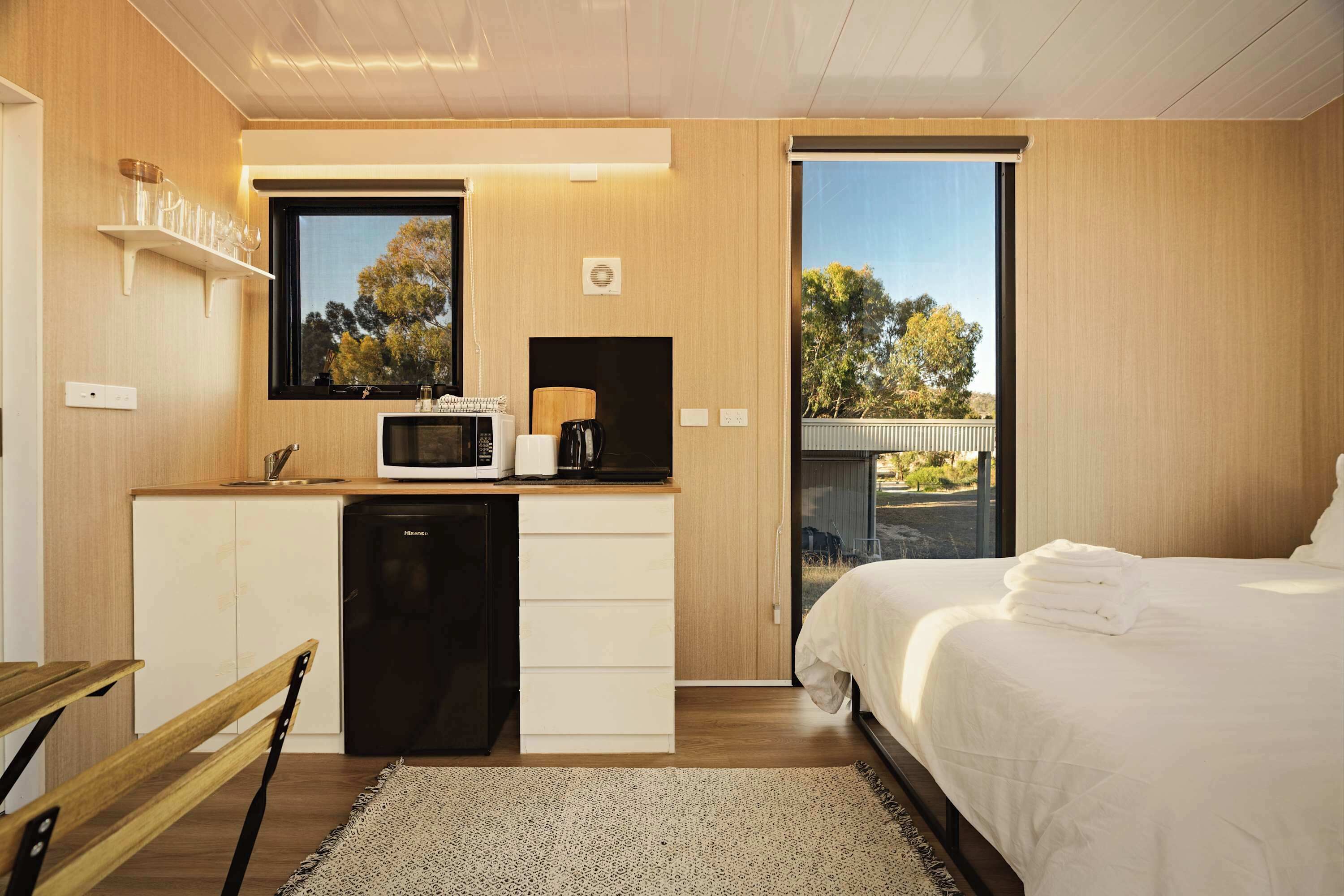 A modern room with a bed, a small kitchenette, a window, and a view of the outdoors.