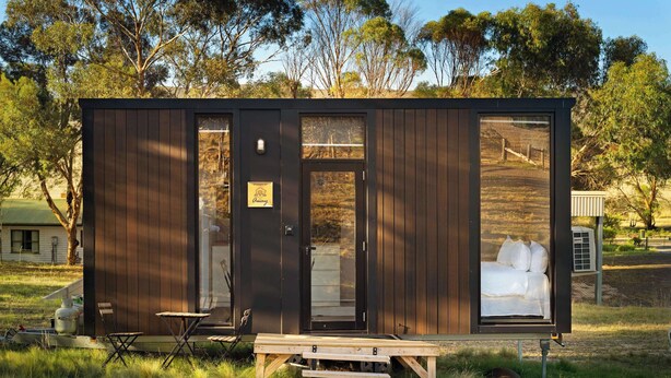 A small cabin with a bed, a table, and a chair outside. - Rowsley Valley Tiny House 2 by Tiny Away (Glenmore)