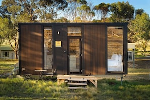 A small cabin with a bed, a table, and a chair outside.
