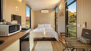 A modern bedroom with a bed, a desk, a microwave, and a view of the outdoors. - Rowsley Valley Tiny House 2 by Tiny Away (Glenmore)