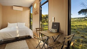 A modern bedroom with a bed, a wooden table, and a view of a green landscape. - Rowsley Valley Tiny House 2 by Tiny Away (Glenmore)
