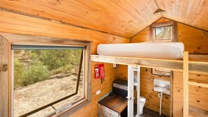 Une petite cabane en bois avec un lit superposé, une petite fenêtre et un lavabo.