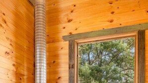 L’intérieur d’une cabane avec un poêle à bois, une fenêtre donnant sur les arbres et une porte menant à l’extérieur.
