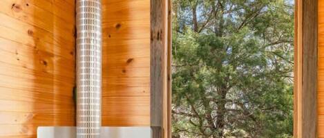 A cabin interior with a wood stove, a window with a view of trees, and a door leading outside.