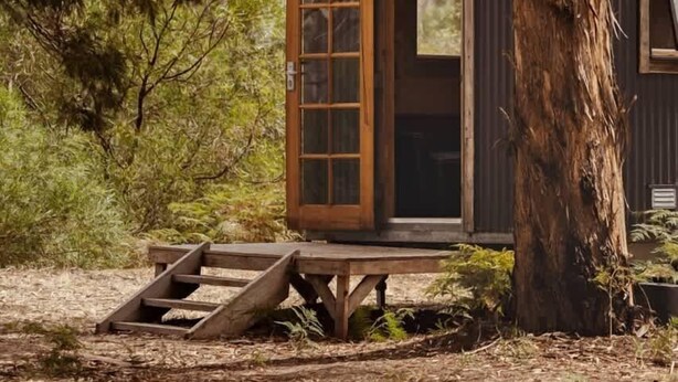 Un chalet rustique avec une porte en bois, entouré d’arbres et doté d’une terrasse en bois.