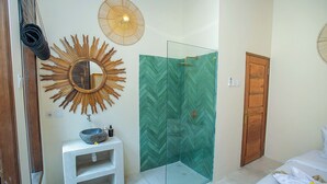 Une salle de bain avec une douche en verre, une porte en bois, un lavabo blanc et un miroir orné d’un motif en forme de soleil.