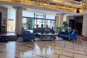 En lobby med et ternet gulv, et sofabord, blå sofaer og en lysekrone.