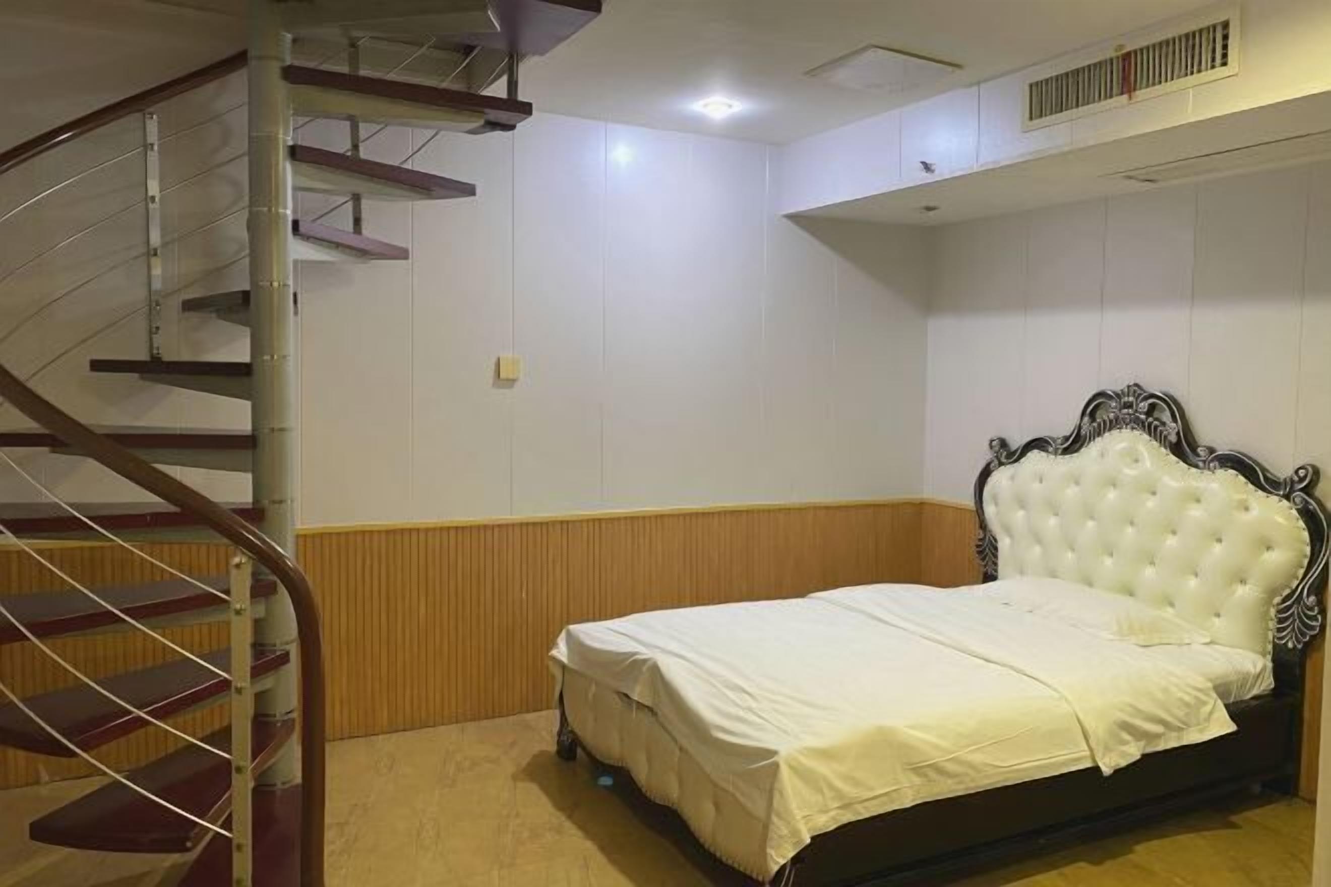 A bedroom with a bed, a wooden floor, a white wall, and a spiral staircase.