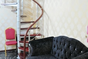 Eine Wendeltreppe, ein roter Sessel und eine schwarze Couch in einem Raum mit ornamentalem Wandpapier.