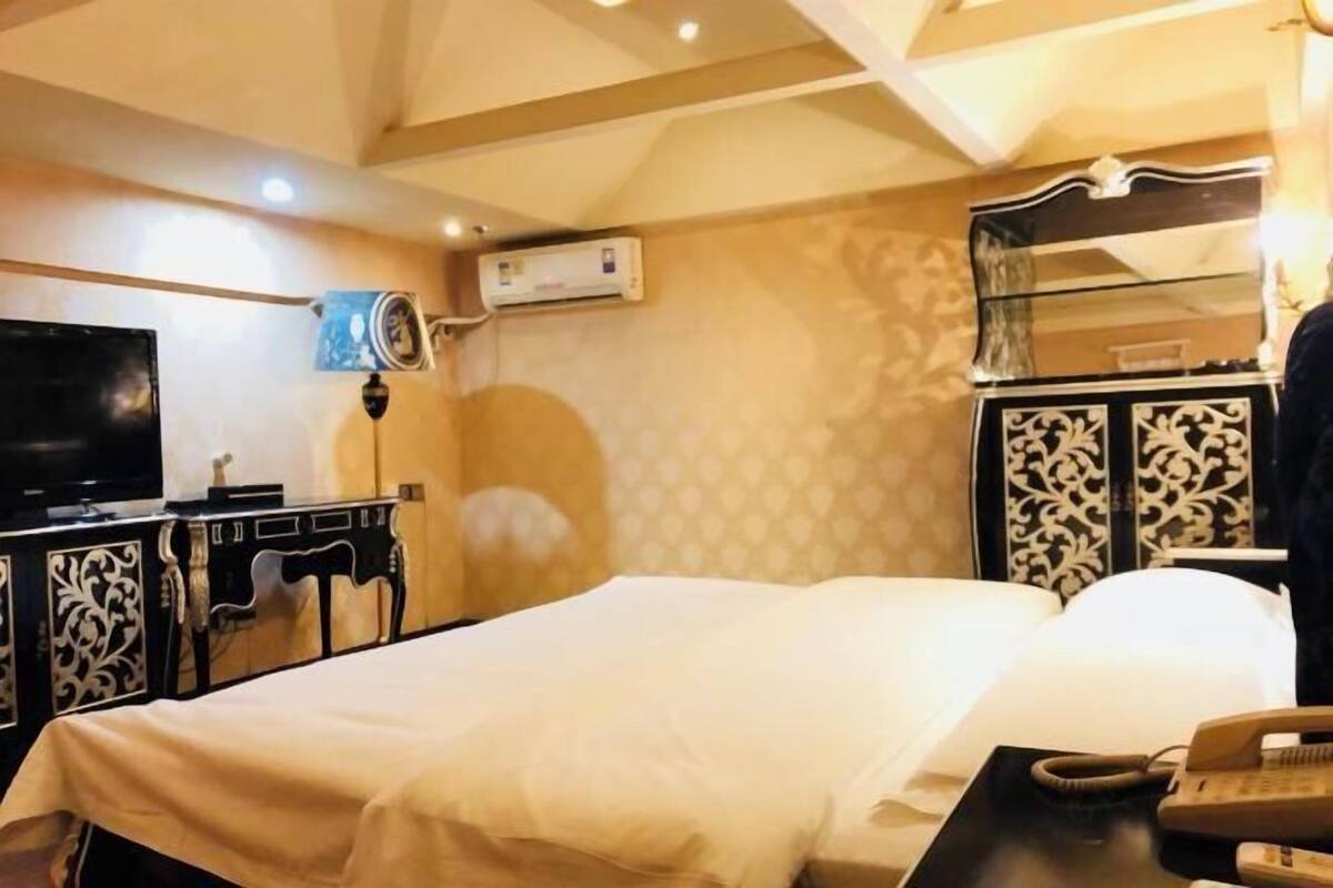 Une chambre d’hôtel comprenant un lit, un bureau avec un téléphone, un appareil de climatisation, une télévision et un miroir décoratif.