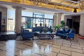 Un hall d’entrée avec un sol à carreaux, une table basse, des canapés bleus et un lustre.