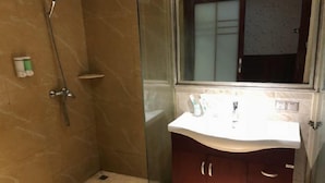 A bathroom with a glass shower enclosure, a white sink, and a wooden cabinet with drawers. - Wuhu Vienna Boutique Hotel (Wuhu)
