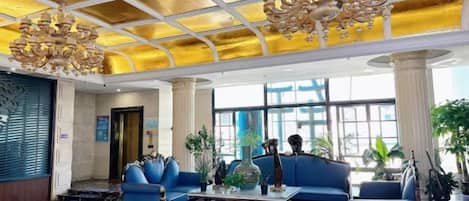 A hotel lobby with a high ceiling, blue sofas, a large chandelier, and large windows.