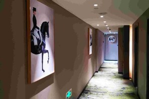 A hallway with framed artwork on the walls, a carpeted floor, and a ceiling with recessed lighting. - MILA HOTEL (Shanghai)