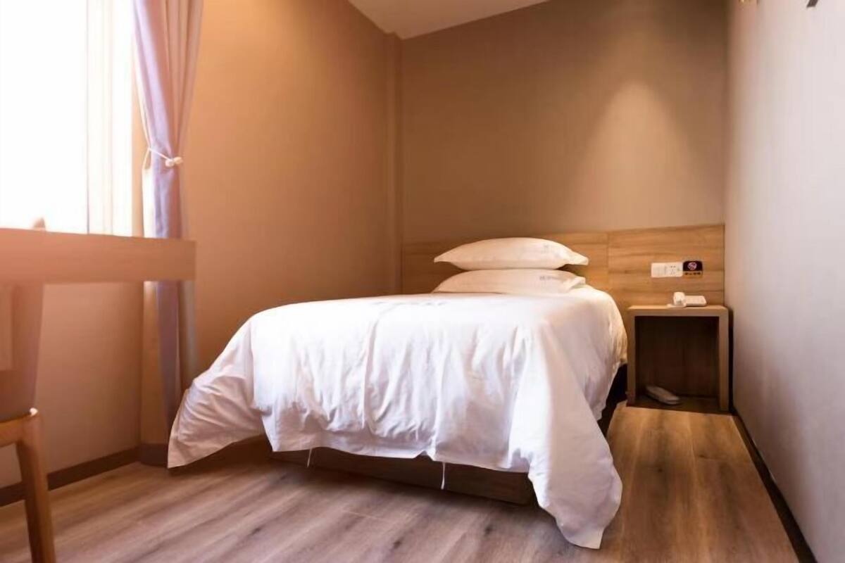 Et hotelværelse med en seng, et natbord, trægulv og et vindue med gardiner.