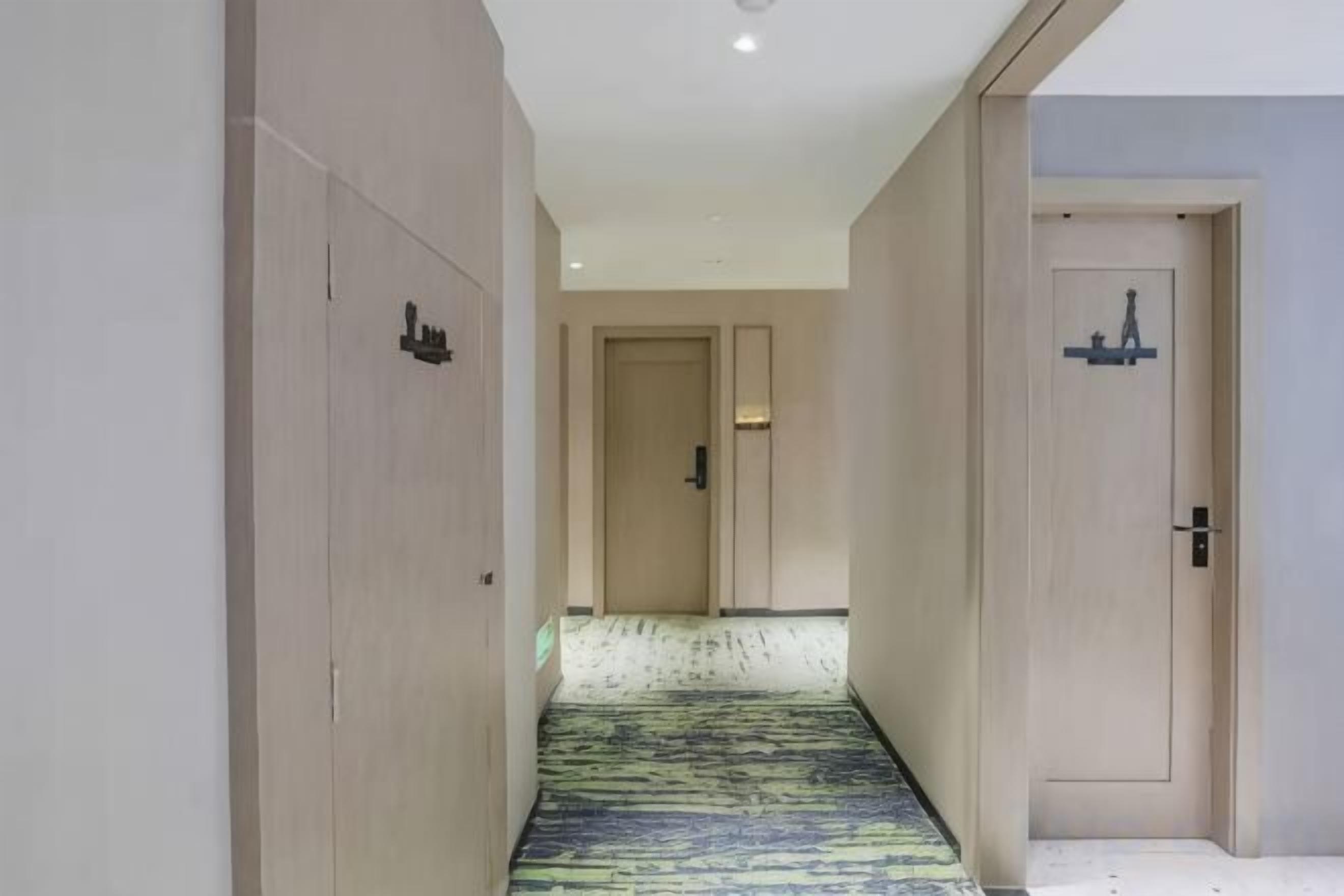 A hotel corridor with a patterned carpet, wooden doors, and a light-colored wall.