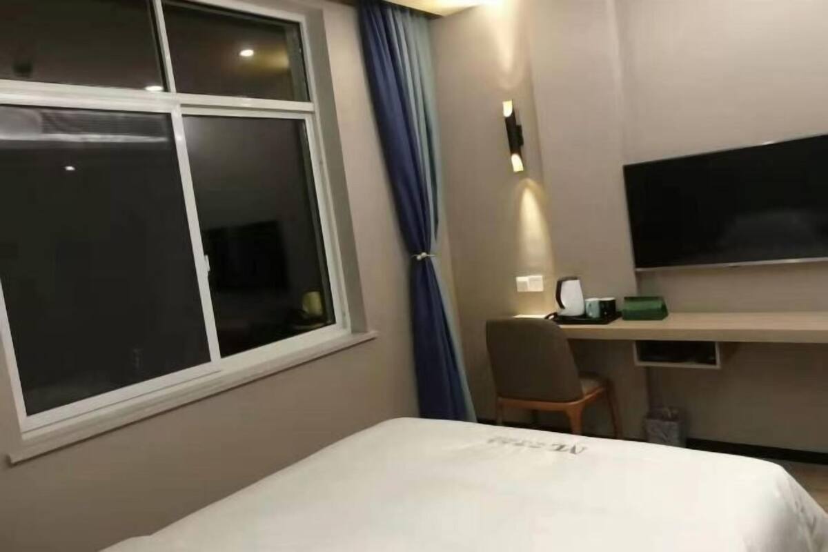 Et hotelværelse med seng, skrivebord, stol, fjernsyn og et vindue med gardiner.