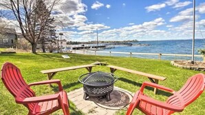 Un patio con un brasero, dos sillas Adirondack rojas y vista a un muelle y al agua.
