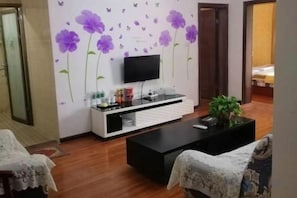 Uma sala de estar com televisão de tela plana em um suporte, mesa de centro preta e sofá com capa branca.