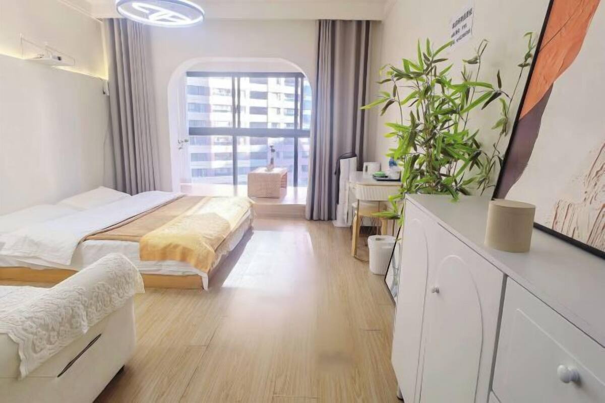 Une chambre d’hôtel avec un lit, une table de chevet, une lampe, une plante en pot et une vue sur les bâtiments par la fenêtre.