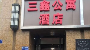 Et hotelskilt med navnet "三鑫公寓酒店" i røde bogstaver mod en brun baggrund.