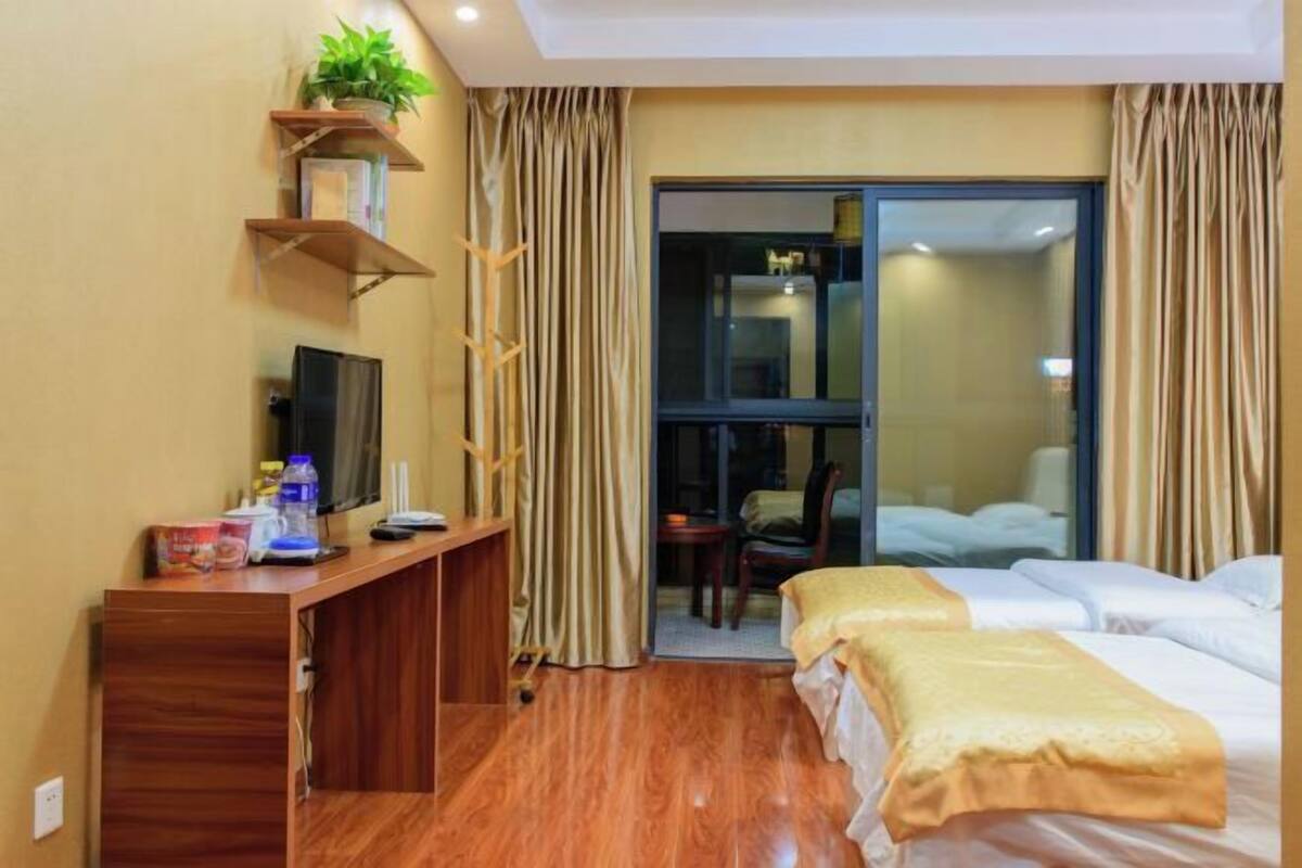 Une chambre d’hôtel avec un bureau en bois, une télévision, deux lits et une porte coulissante donnant sur un balcon.