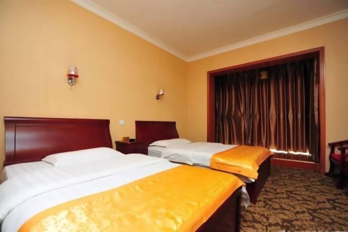 Une chambre d’hôtel avec deux lits, une tête de lit en bois, une table de chevet, une lampe fixée au mur et une fenêtre avec des rideaux.