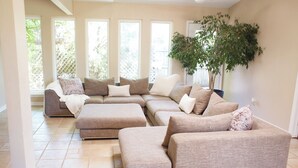 Ein geräumiges Wohnzimmer mit Ecksofa, großen Fenstern und einer Topfpflanze.