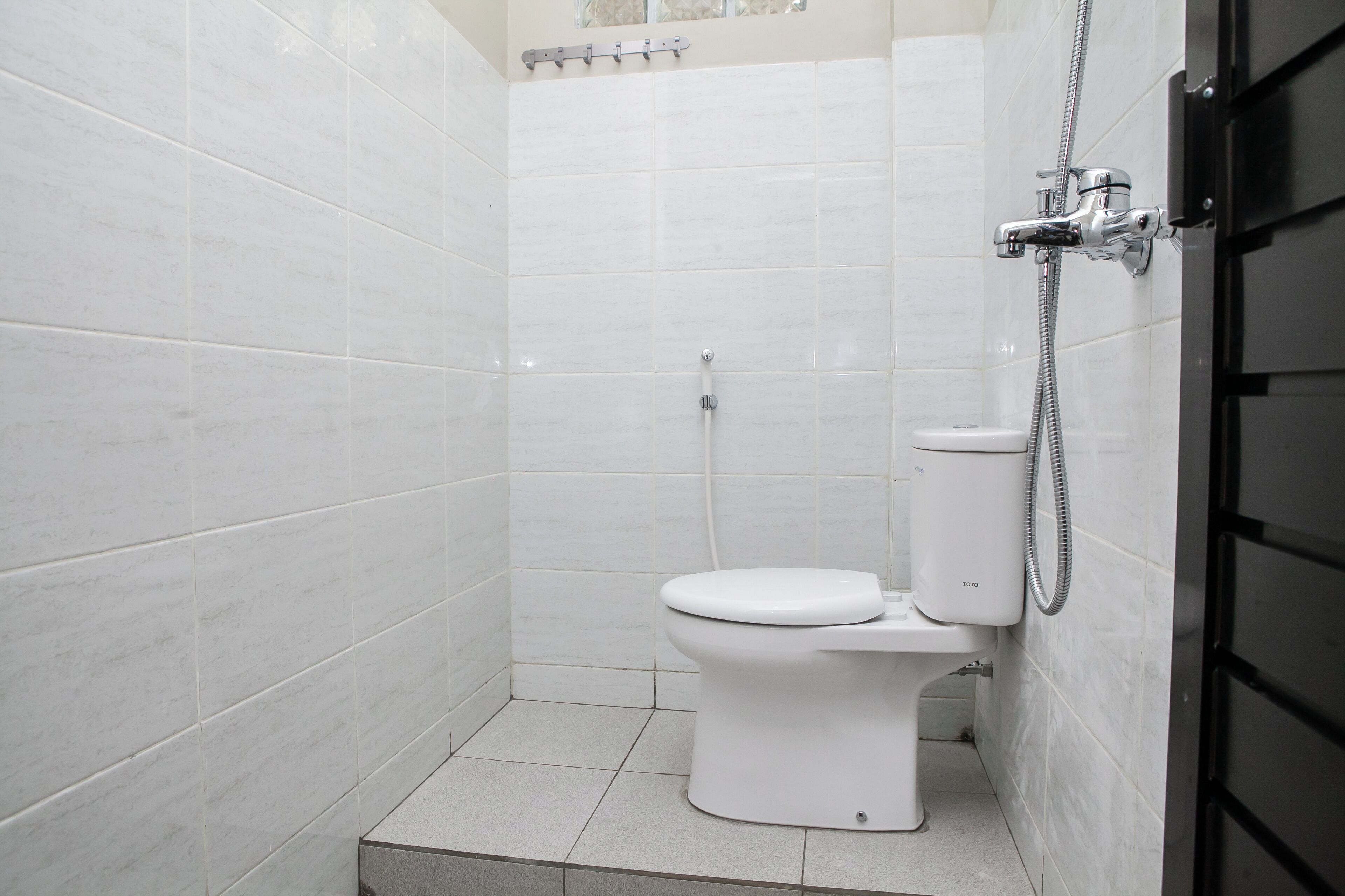 Un baño pequeño y moderno con azulejos blancos, un inodoro y una cabina de ducha.