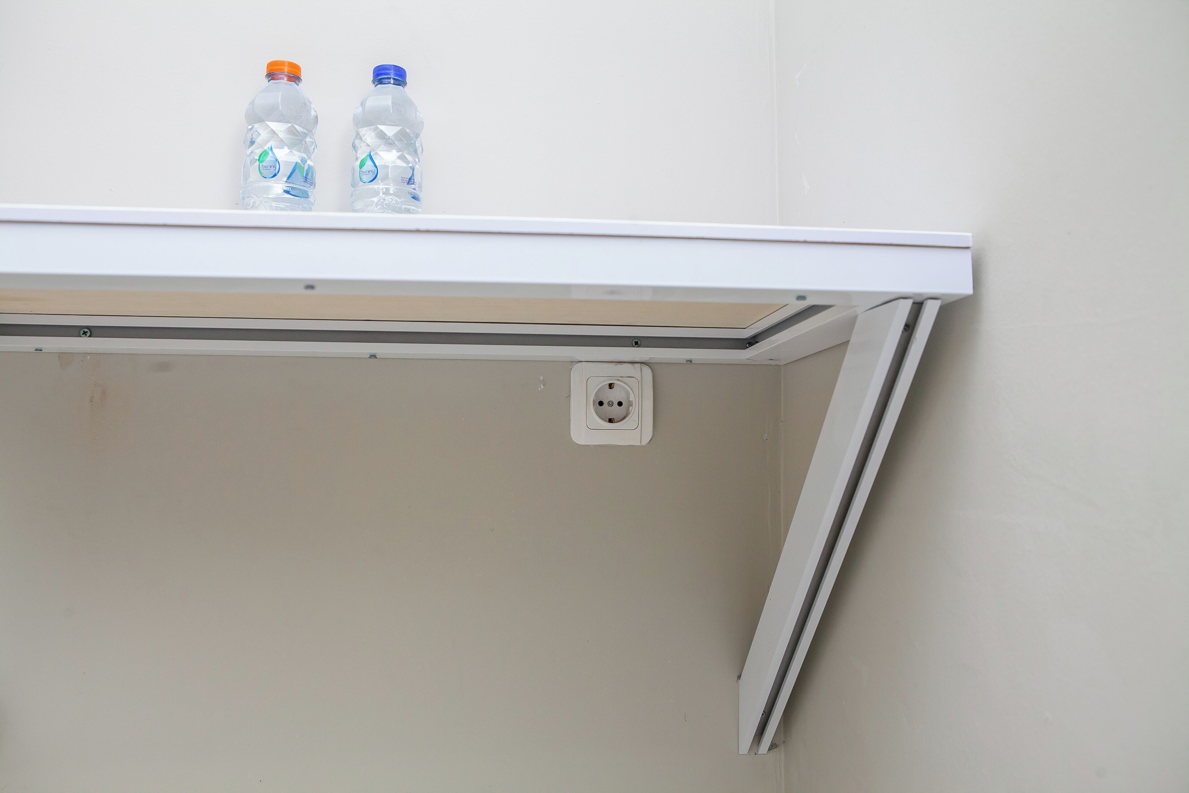 A white shelf with two plastic water bottles and a power outlet.