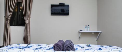 A hotel room with a bed, a TV on the wall, and a small shelf with bottles.