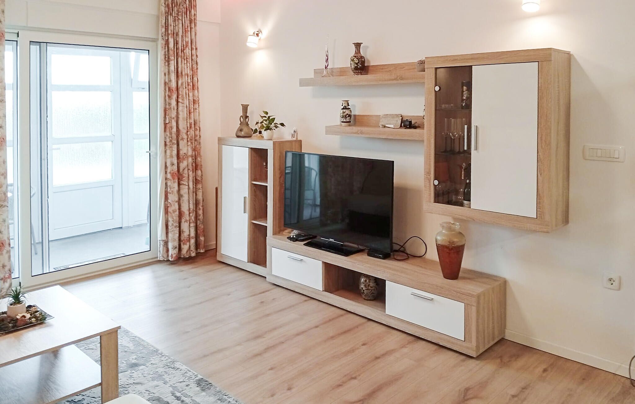 Uma sala de estar moderna com televisão de tela plana, prateleiras de madeira, um armário e uma porta de correr de vidro.