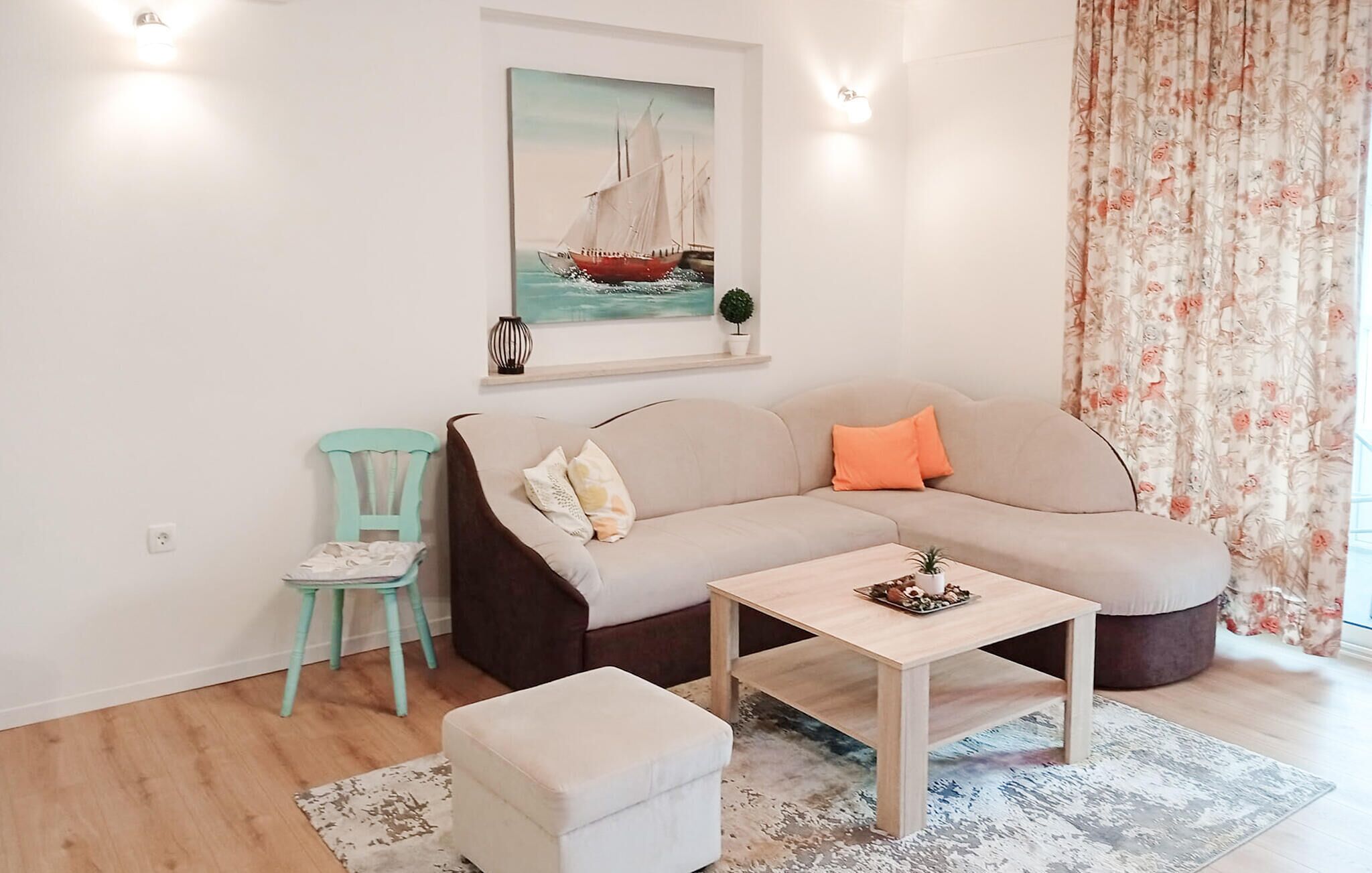 A living room with a sofa, a small table, a chair, a painting, and a floral curtain.
