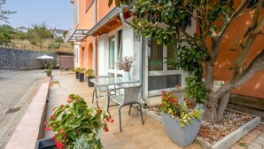 Un patio con mesa y sillas, rodeado de plantas en macetas y un árbol.
