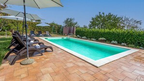 Una piscina rectangular con solárium empedrado, rodeada de sillones de descanso y sombrillas.