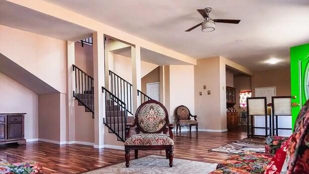 A spacious living room with a high ceiling, a staircase, and a green door.