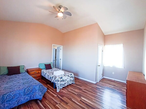 Un dormitorio con cama, mesita de noche, cómoda, ventilador de techo y puerta.
