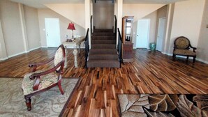 A spacious living room with hardwood floors, a grand staircase, and a large window.