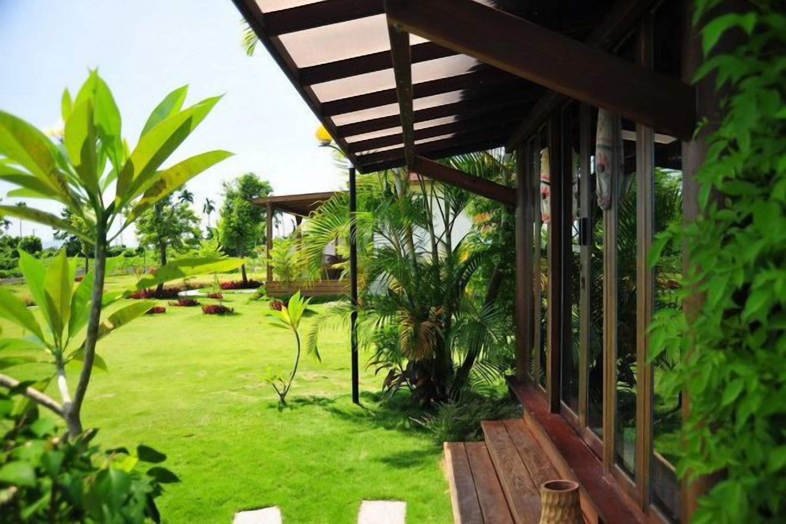Un espacio al aire libre cubierto con un banco de madera, abundante vegetación y vistas despejadas a un jardín.