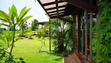 Un espacio al aire libre cubierto con un banco de madera, abundante vegetación y vistas despejadas a un jardín.