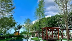 A serene outdoor area with a clear blue sky, a calm water feature, and wooden gazebos. - Bali Hostel (Hualien)