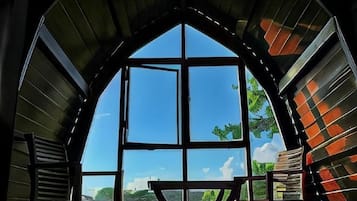 Una habitación con un amplio ventanal arqueado, una mesa de madera y vista a un paisaje verde.