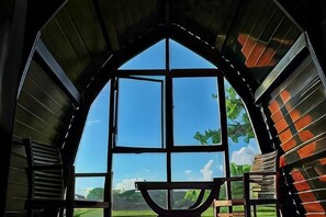 A room with a large arched window, a wooden table, and a view of a green landscape. - Bali Hostel (Hualien)