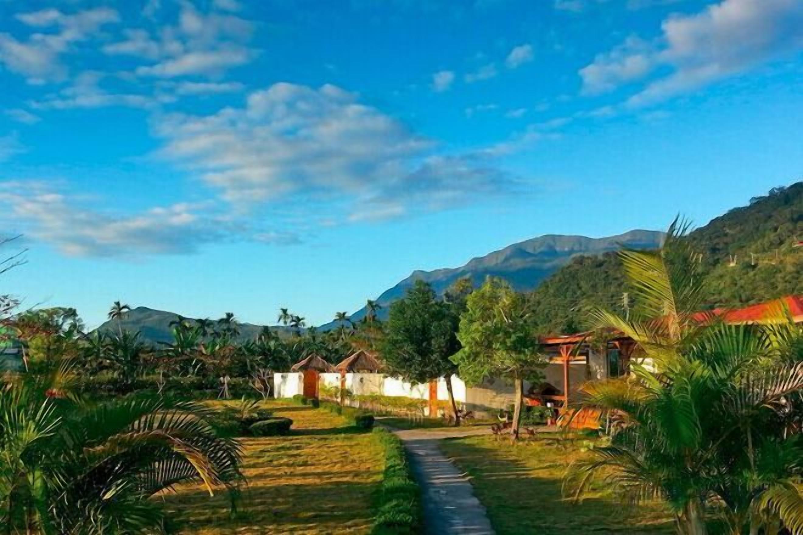 Un sendero que lleva a un edificio rodeado de vegetación y montañas al fondo.