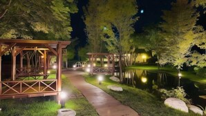 A nighttime scene with a wooden gazebo structure, a pathway, and a pond. - Bali Hostel (Hualien)