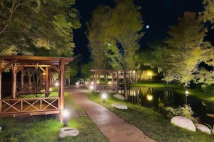 Escena nocturna con una estructura de pérgola de madera, un camino y un estanque.