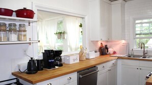 Una cuina moderna amb armaris blancs, un taulell de fusta, un rentaplats i una cafetera.