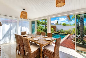 A dining area with a pool view, wicker chairs, and a wooden table. - VILLA MAÏDIANA - villa 10 pers. piscine chauffée à 200 m du lagon de La Saline-les-Bains (Saint-Gilles-Les-Bains)